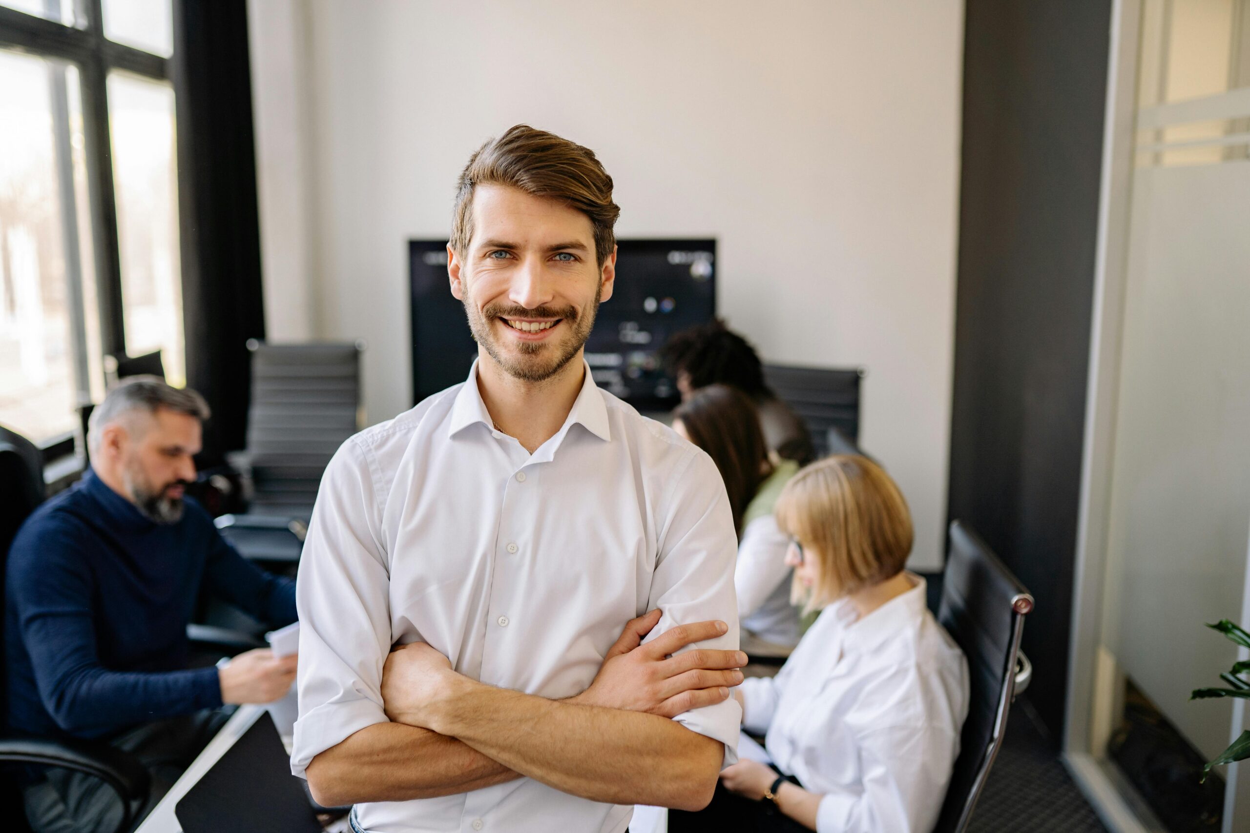 Home Smiling businessman standing confidently with arms crossed in an office setting.